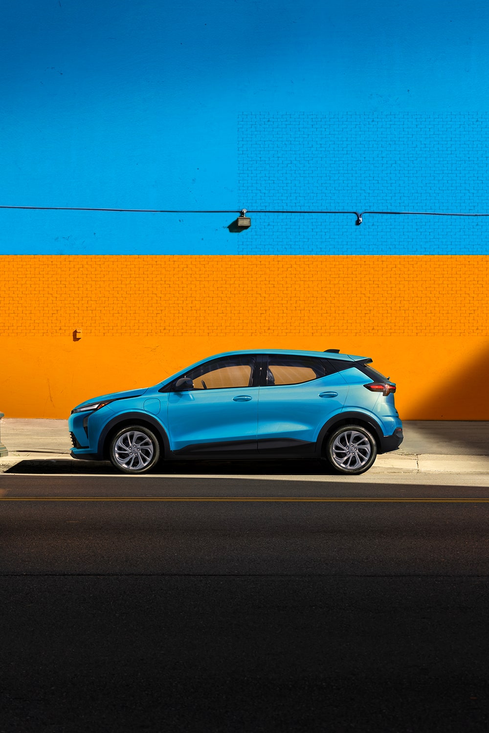 A Light Blue 2027 Chevrolet Bolt is Shown in a Side Profile View, with the Text "Bolt Gets Bolder," and Highlights of its New Front and Rear Fascia, 17" Aluminum Wheels, and Gloss Black Outside Mirrors.