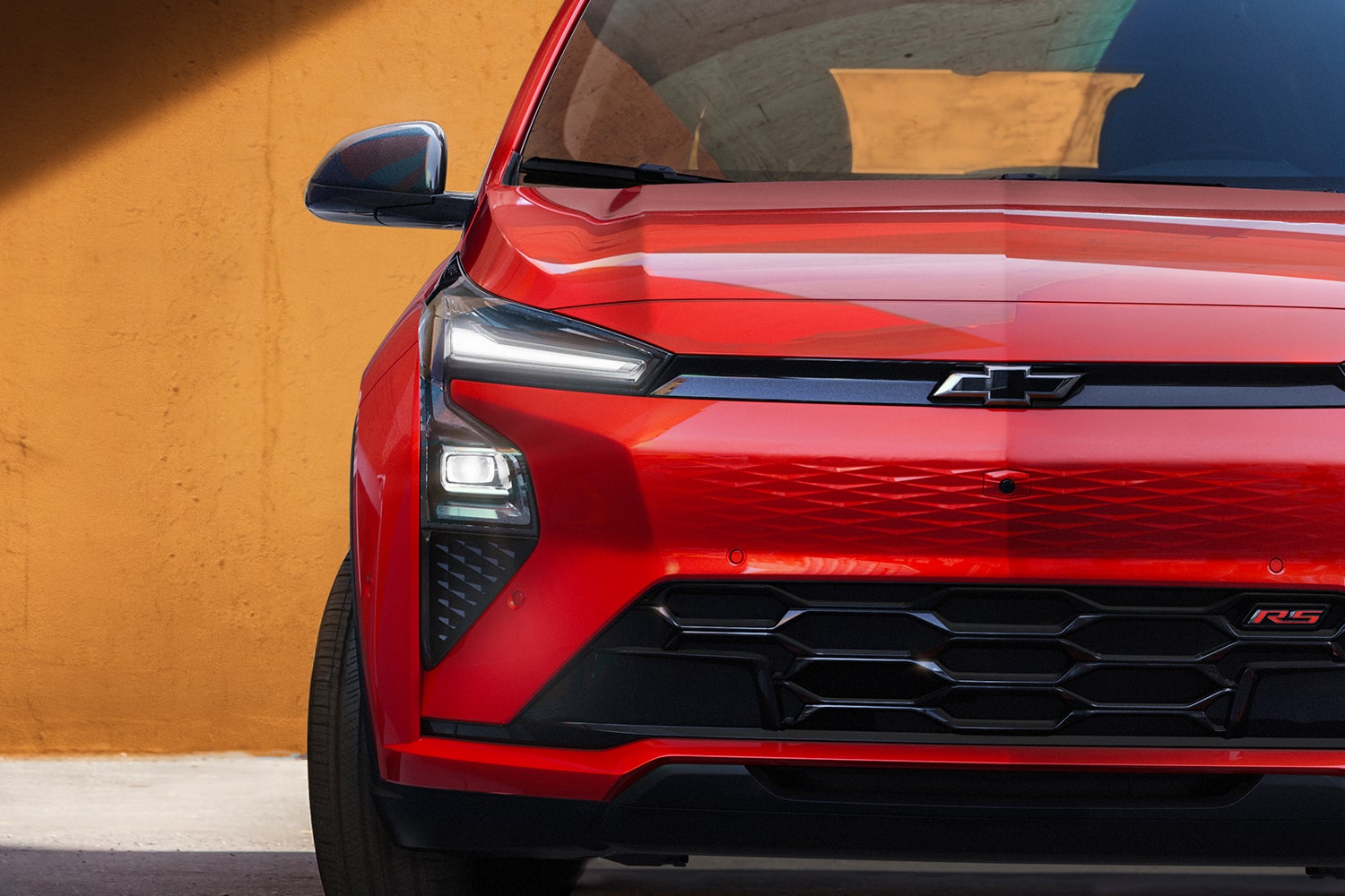 A Close-Up of the Front of a Red 2027 Chevrolet Bolt RS, Showing the Headlights, Black Grille, and the RS Badge.
