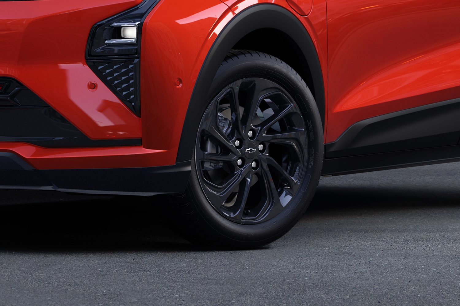 A Close-Up of the Front Wheel of a Red 2027 Chevrolet Bolt RS, Showing the Black Multi-Spoke Wheel with a Black Chevrolet Bowtie in the Center.