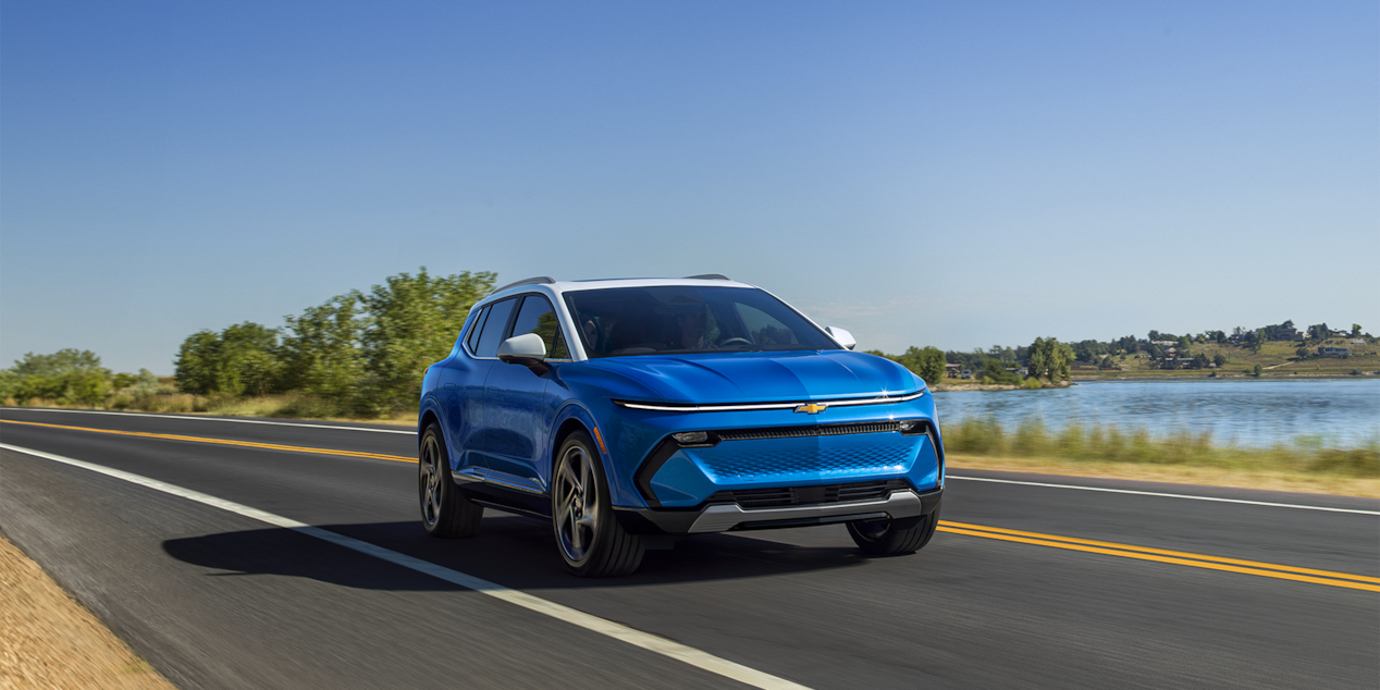 A Chevrolet Equinox EV driving alone on a road beside a lake.