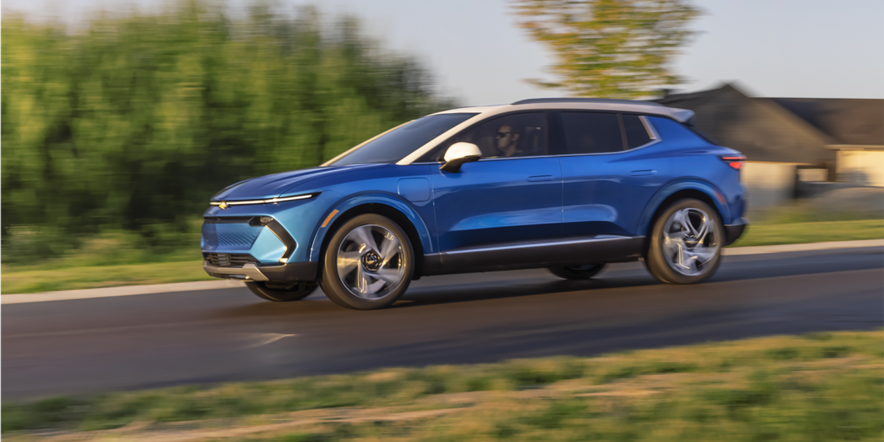 A Chevrolet EV driving down alone on a residential road.