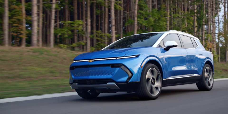 A Chevrolet EV driving alone on a tree-lined road.