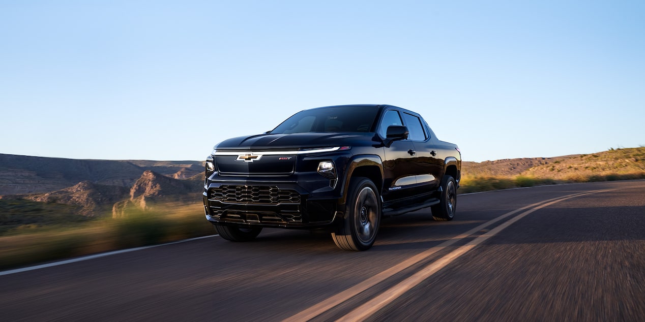 Vue latérale avant du Chevrolet Silverado EV 2025 en mouvement seul sur une route dans une région éloignée.