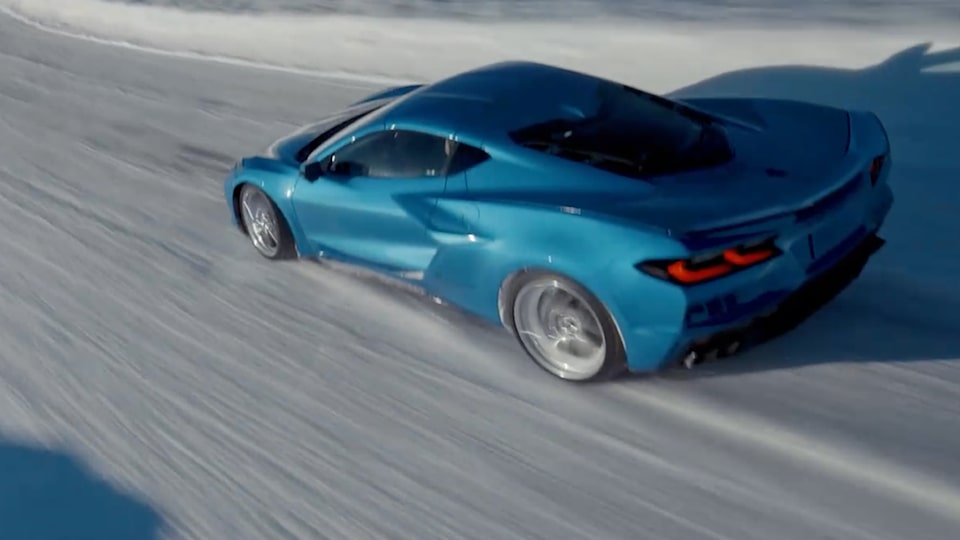 Front Eye Level View of a Blue Chevrolet Corvette E-Ray Going Down the Road Surrounded by Snow.