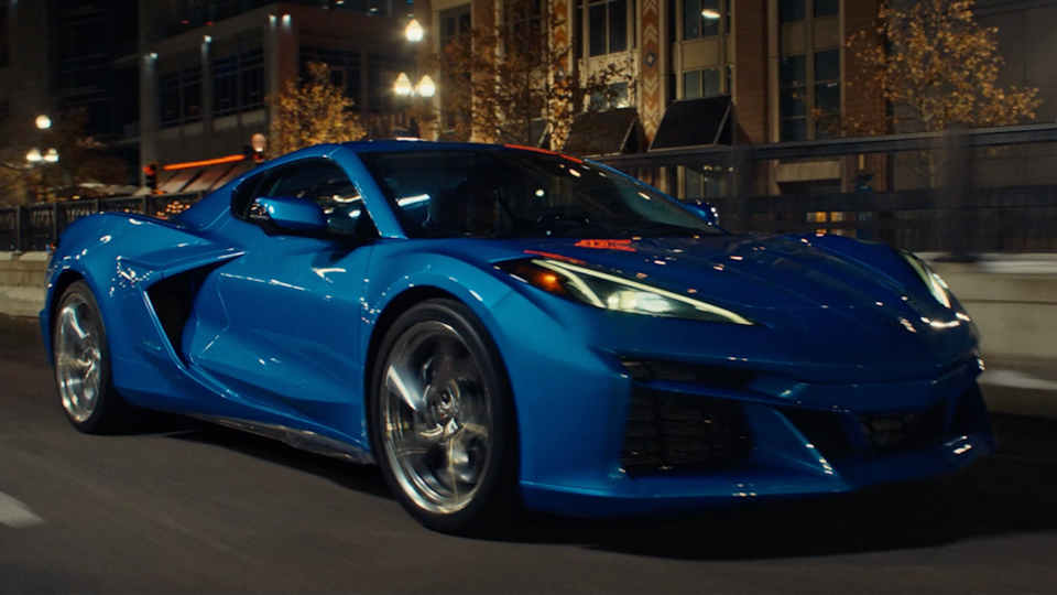 View of a Blue Chevrolet Corvette E-Ray Driving Down the Road at Night.