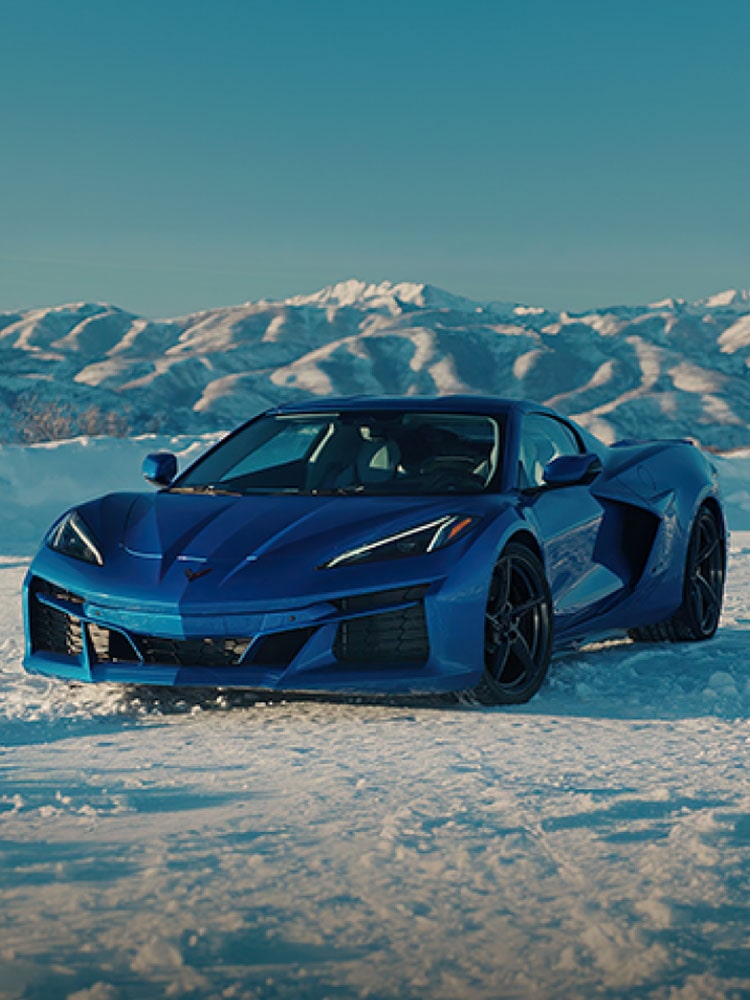 Three Quarters View of a 2026 Blue Chevrolet Corvette E-Ray in an Icy Plain Surrounded by Icy Mountains.