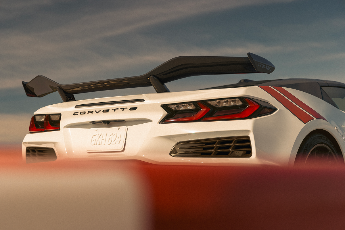A White 2027 Chevrolet Corvette Grand Sport Speeds Through a Sunlit Corner, Showing Its Sculpted Side Air Intake, Black Wheels, and Red Accent Stripes.