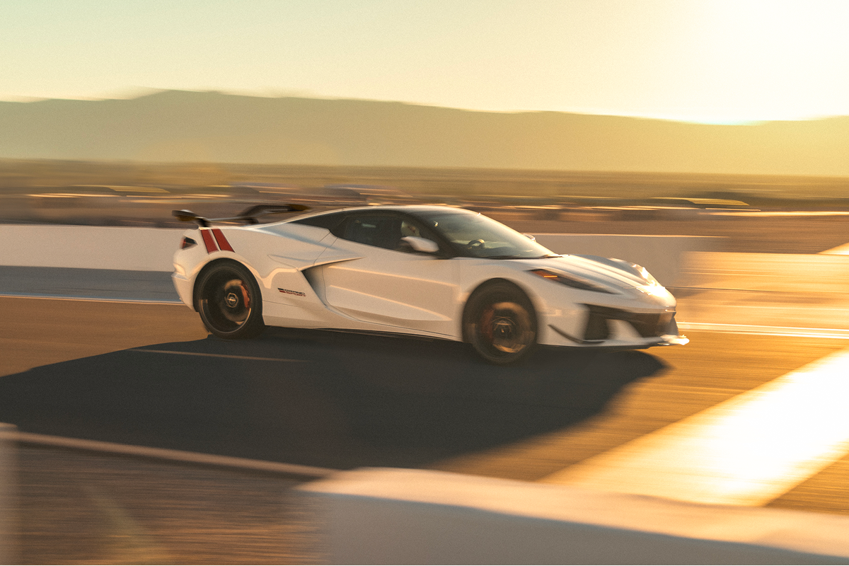 Side View of a White 2027 Chevrolet Corvette Grand Sport Driving Along a Racetrack at Sunset.