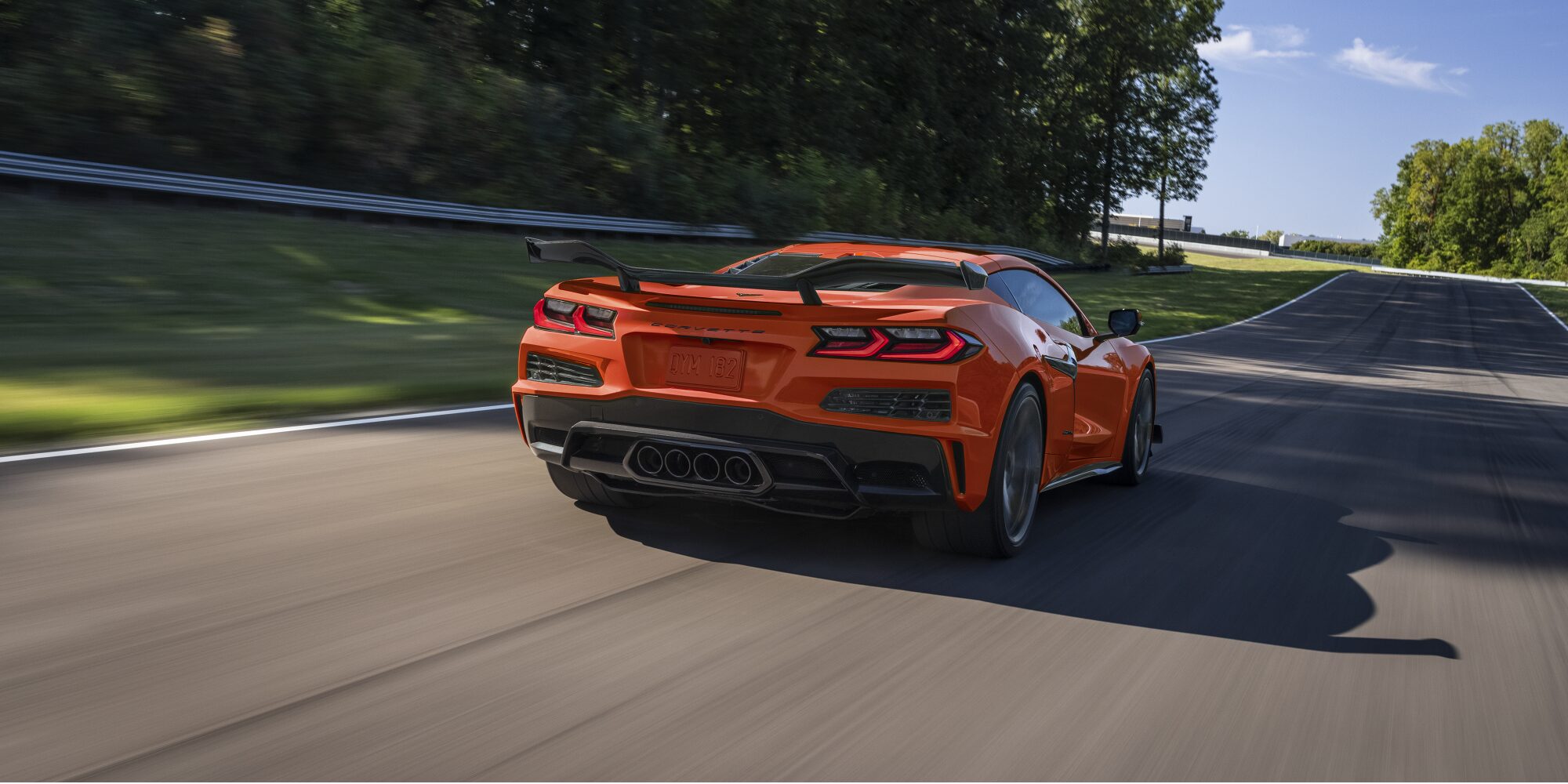 Vue arrière de la Chevrolet Corvette Z06 2027 roulant à vive allure sur une route bordée d'arbres.