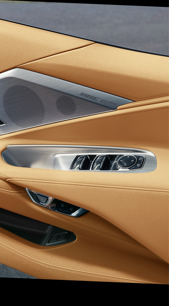 Gros plan sur le panneau de porte intérieur en cuir fauve d'une Chevrolet Corvette Z06 2027, avec des commandes argentées et un haut-parleur Bose.