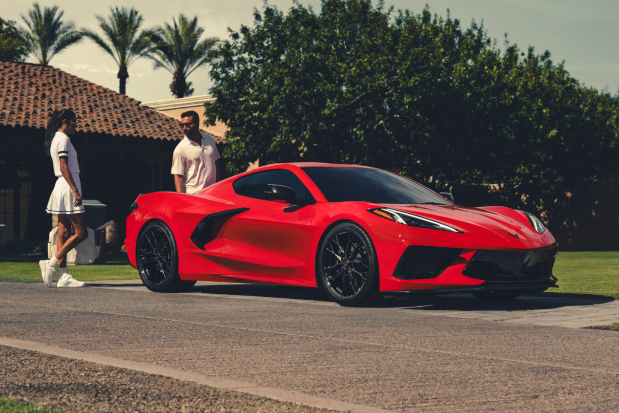 A Couple Standing Next To Red Corvette Stingray