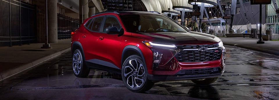 A Chevrolet SUV covered by a GM Protection Plan parked by the sidewalk with its headlights on.