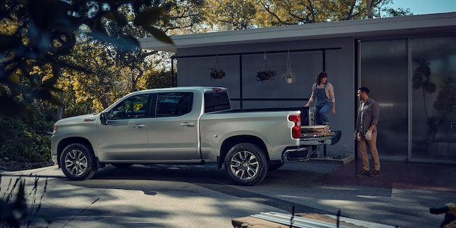 Two persons loading supplies into the back of a Chevrolet Silverado 1500.