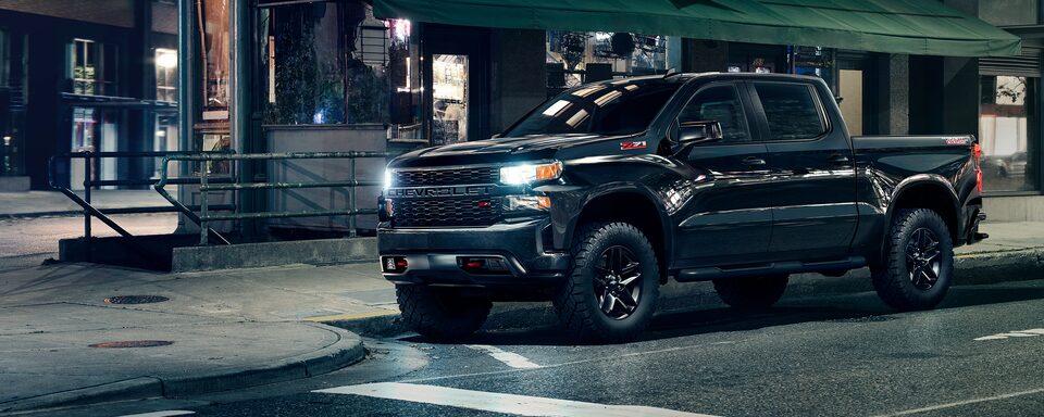 Front driver shot of the 2023 Chevrolet Silverado Custom Trail Boss Midnight Edition with headlamps on.