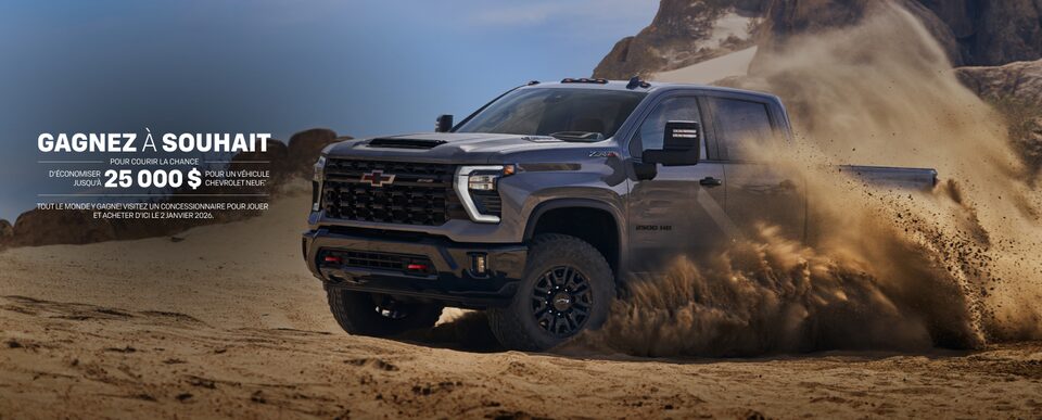 Vue latérale avant du pick-up Chevrolet Silverado HD 2025 en train de déraper sur un terrain sablonneux.