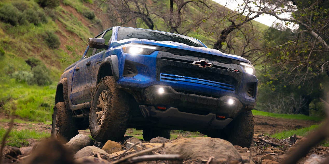 Low Angle Front View of a 2026 Blue Chevrolet Colorado Driving Through a Rocky Road in a Forest.