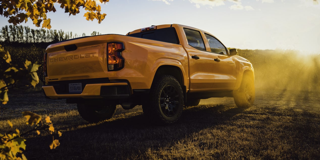 Three Quarters Rear View of a Yellow 2026 Chevrolet Colorado Parked on a Grassy Plain.