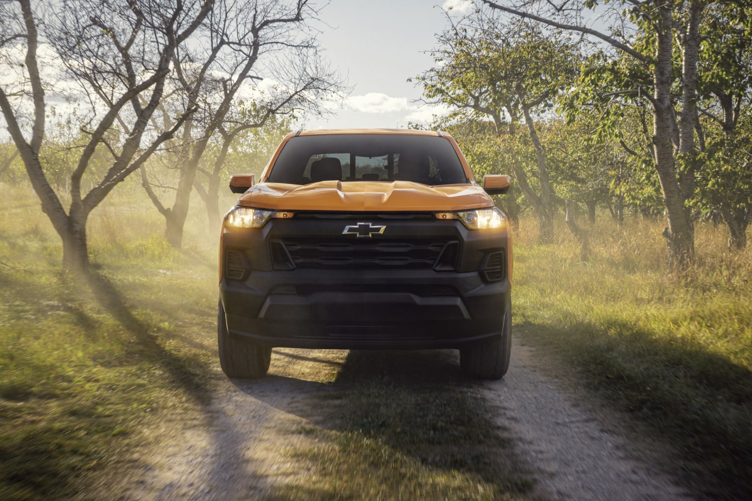 Front View of a Yellow 2026 Chevrolet Colorado Pickup Truck Driving Down a Road with Trees on Both Sides.