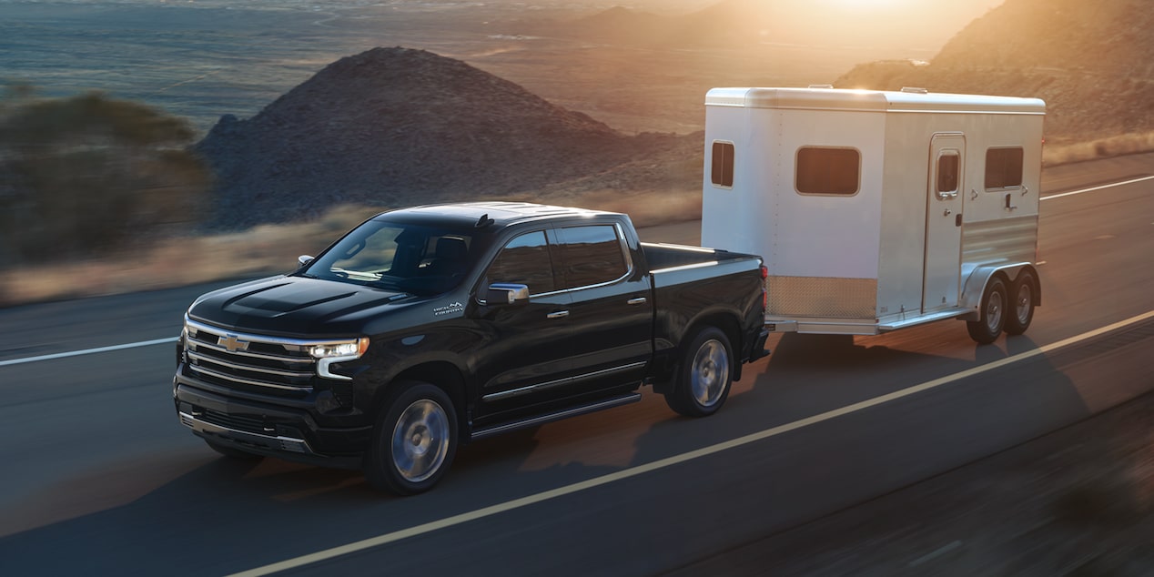 Le Chevrolet Silverado LD 2026 qui tire une remorque sur une route au bord de l’eau.