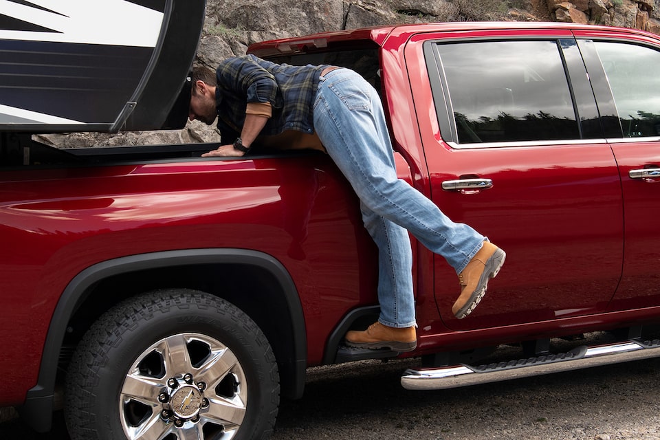 Un homme utilise le marchepied latéral extérieur du camion Chevrolet 2021 Silverado HD pour accéder plus facilement au compartiment de rangement.