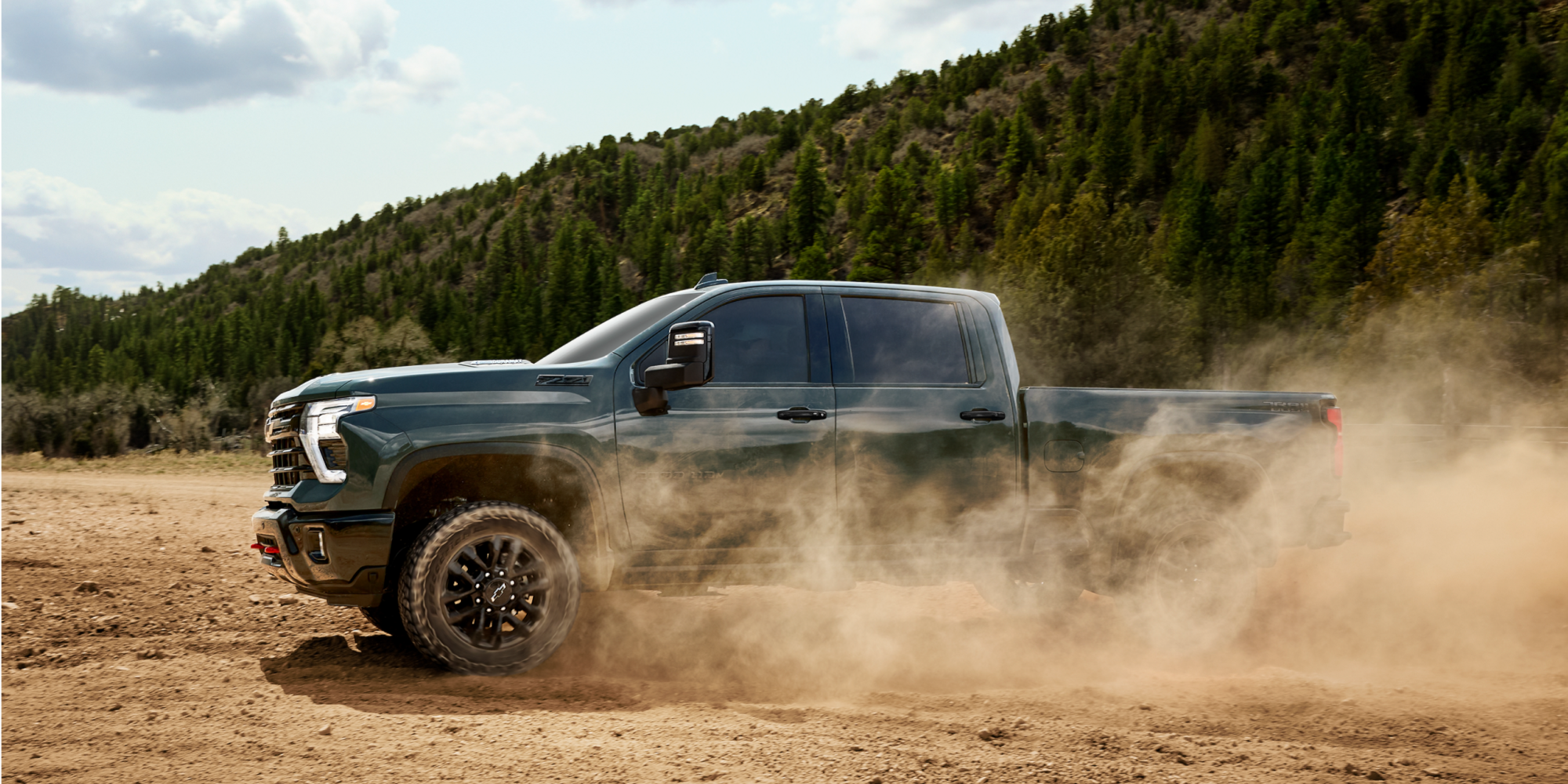 Chevrolet Silverado HD Trail Boss Driving Near a Forest on a Dusty Road