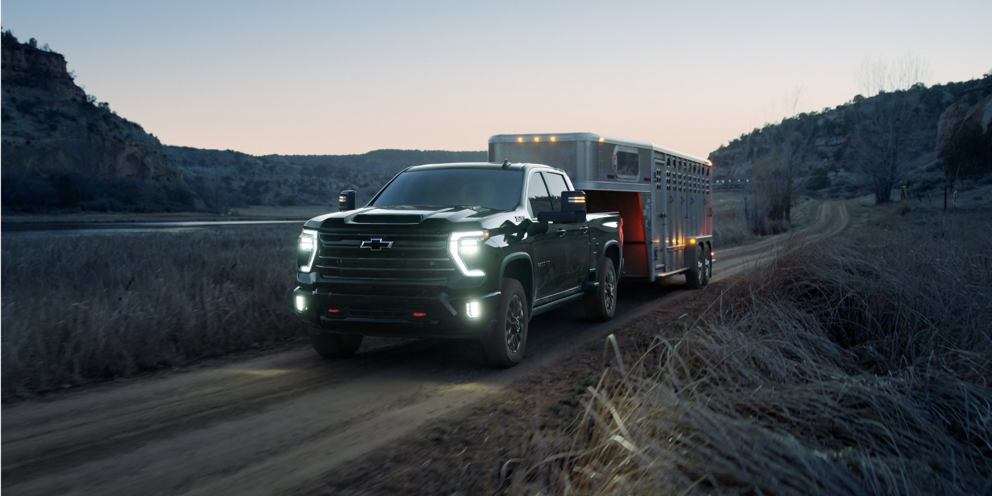 Chevrolet Silverado HD Trail Boss Towing an Animal Trailer Down a Highway at Dusk.