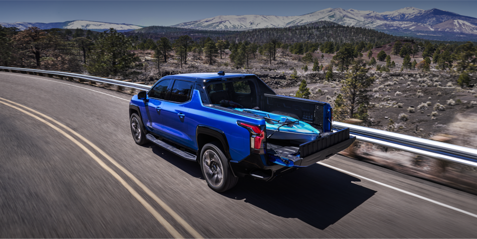 2024 Chevrolet Silverado EV driving on a highway with a kayak stowed in the bed.