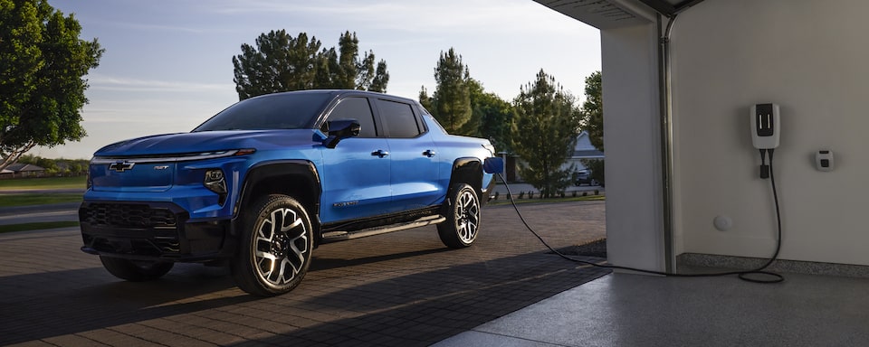 2024 Chevrolet Silverado EV parked outside a garage while plugged into a charging station.