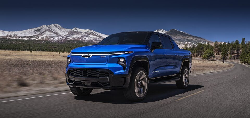2024 Chevrolet Silverado EV driving on a road with mountains in the background.