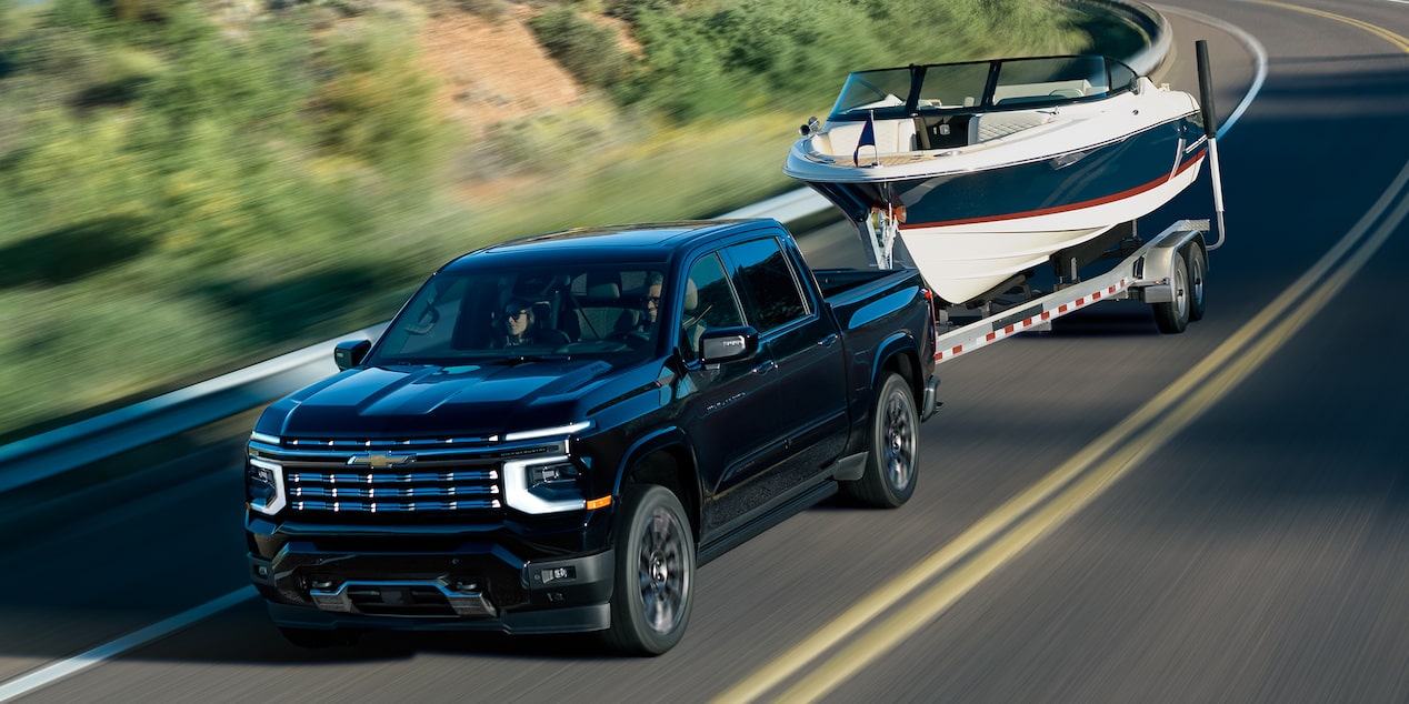 A Next-Generation 2027 Silverado 1500 Truck towing a boat on the road on a sunny day.