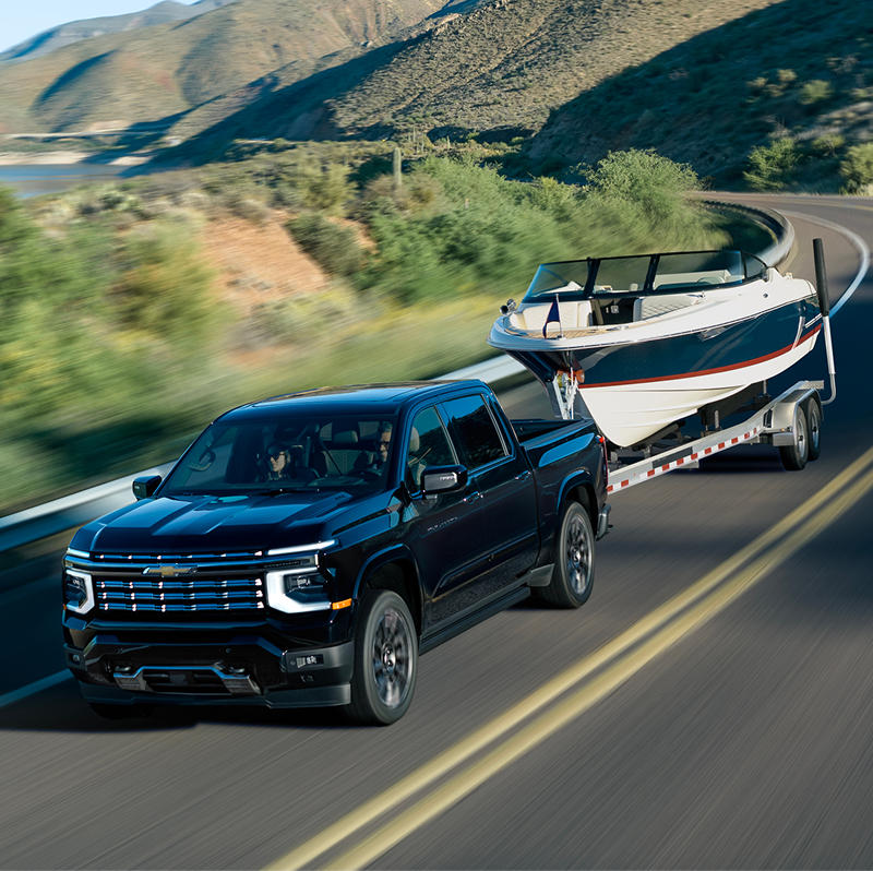 2027 Chevrolet Silverado 1500 High Country towing a boat on a winding mountain road