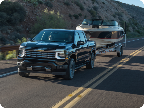 2027 Chevrolet Silverado 1500 High Country towing a boat along a mountain highway