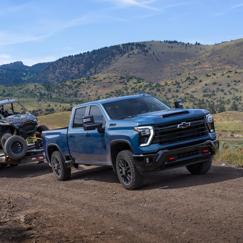Le nouveau pick-up Chevrolet Silverado HD 2027 remorque une grande remorque à plateau chargée de véhicules à travers un paysage désertique.