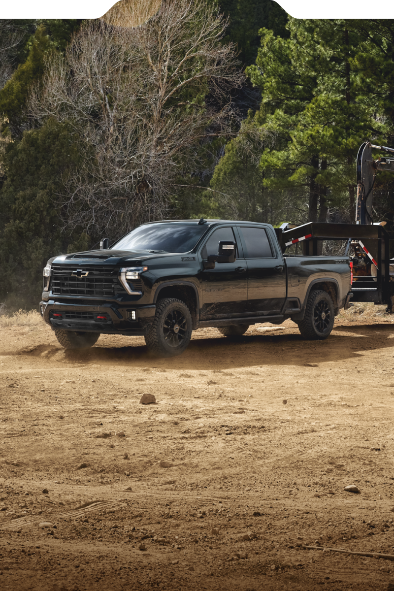 Le nouveau camion Chevrolet Silverado HD 2027 remorque une remorque à plateau transportant une pelle compacte à travers un chantier poussiéreux.