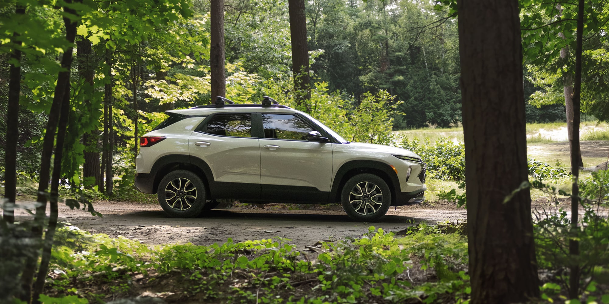 Side profile of a white 2027 Chevrolet Trailblazer parked along a forest trail.