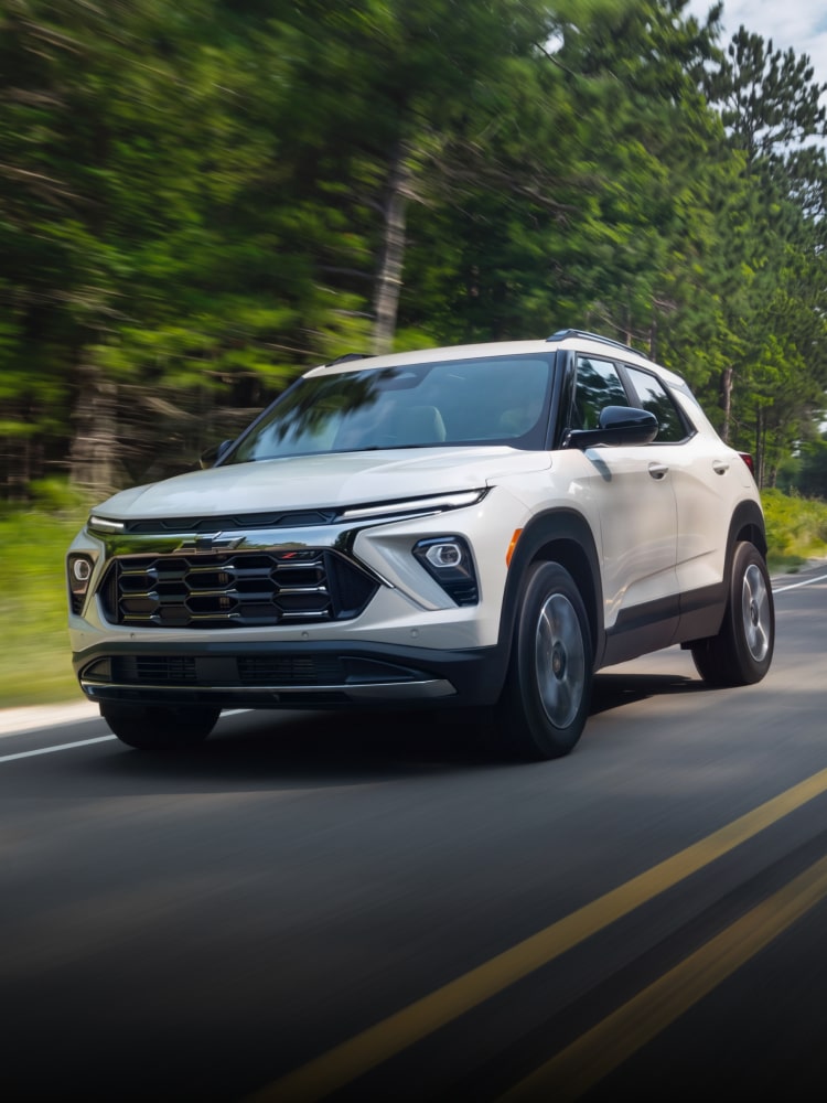 Front three-quarters view of a 2027 Chevrolet Trailblazer Driving on a Road Surrounded by Trees.