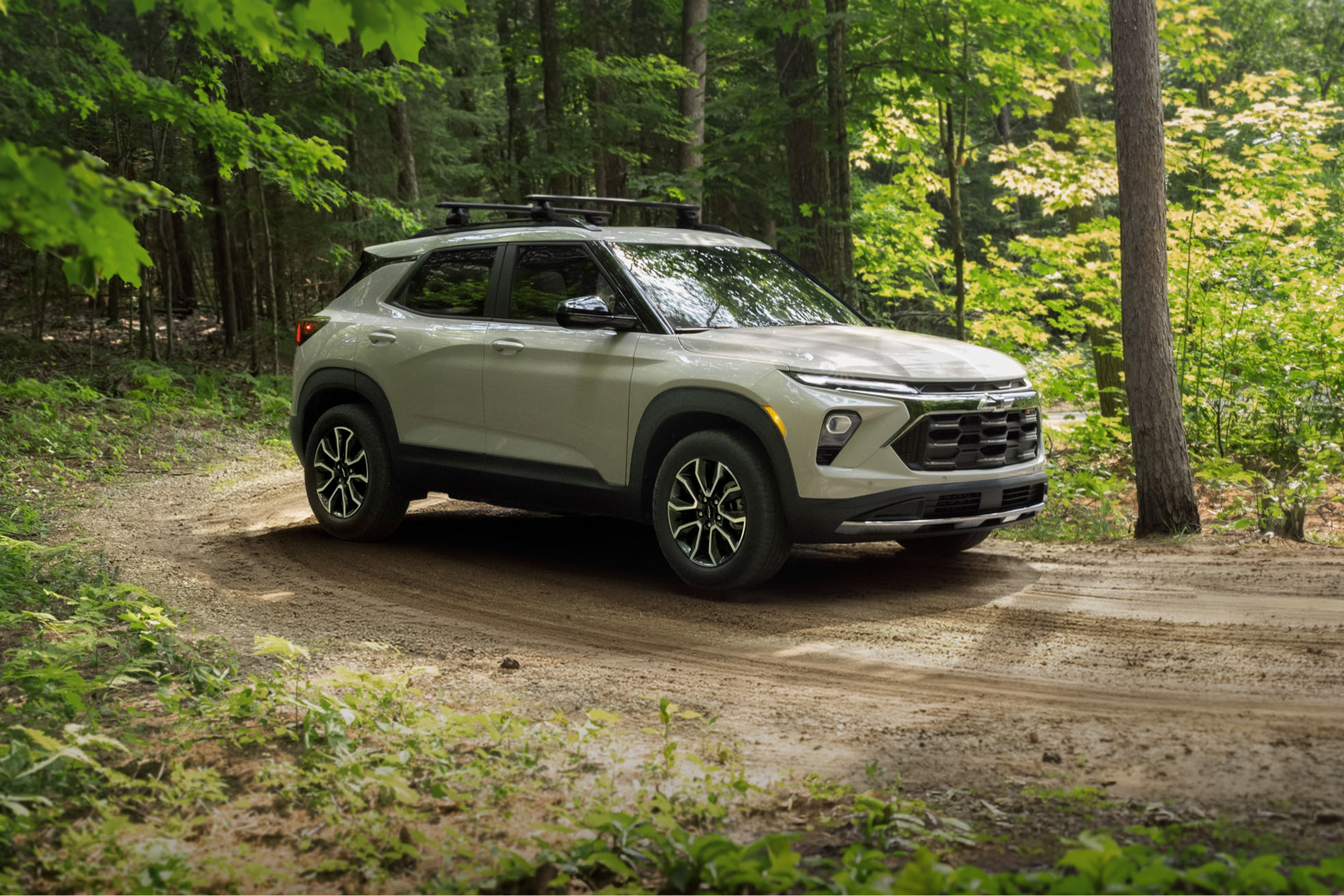 Un VUS Chevrolet Trailblazer 2027 roulant sur un sentier de terre à travers une forêt verdoyante, entouré de grands arbres et de paysages naturels boisés.