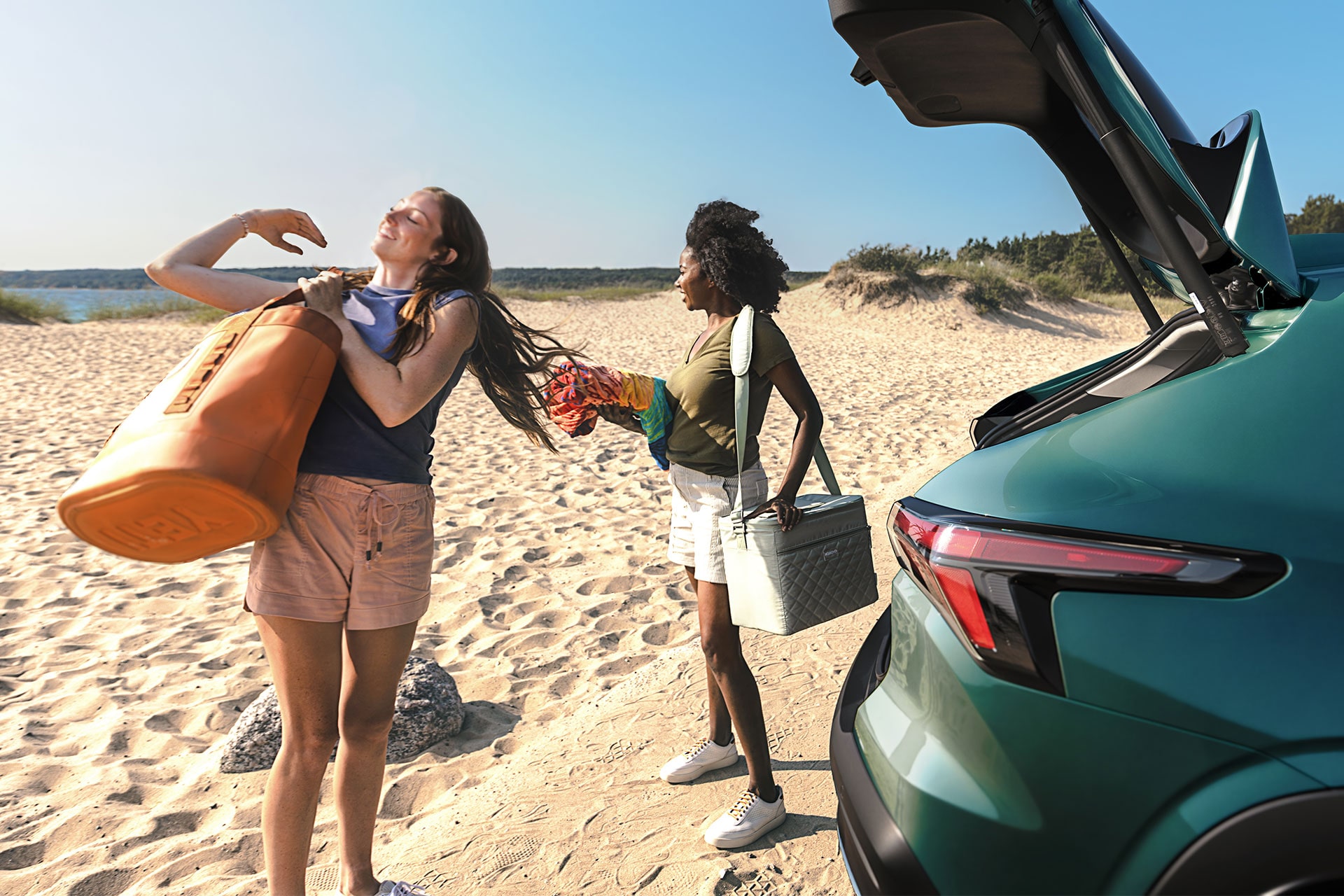 Open rear liftgate of the 2027 Chevrolet Trax small SUV at a beach destination, showing cargo access while beach gear and personal belongings are unloaded from the rear storage area.