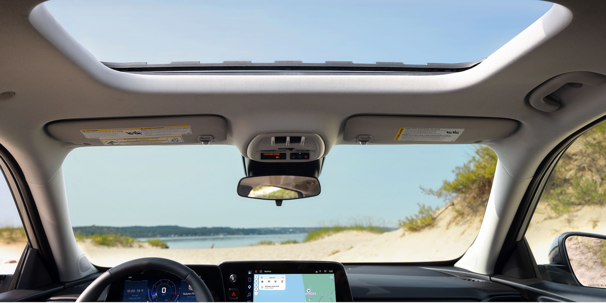 2027 Chevrolet Trax small SUV interior view featuring a panoramic sunroof, digital display screens, and a beach landscape visible through the windshield.