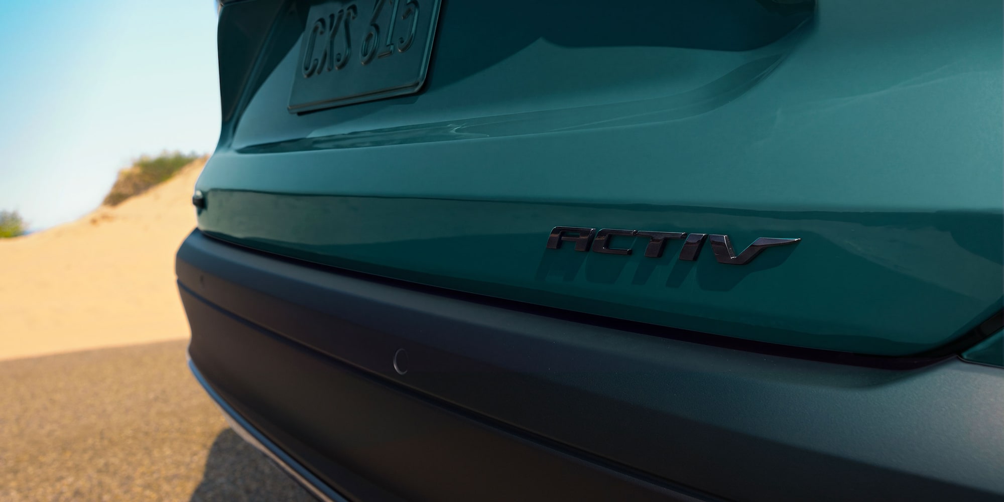 2027 Chevrolet Trax small SUV ACTIV badge displayed on the rear tailgate with teal exterior paint and beach scenery in the background.