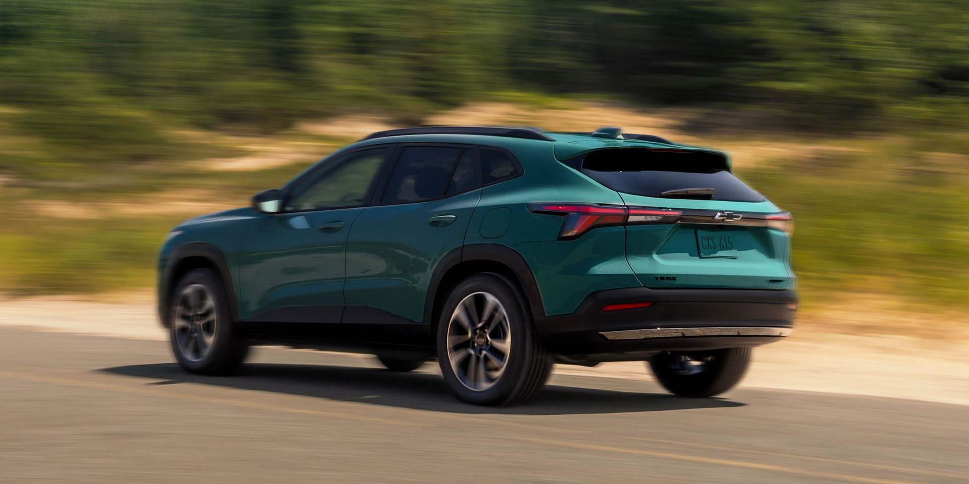Green 2027 Chevrolet Trax small SUV driving on a paved road, shown from a rear three-quarter angle with motion blur highlighting the vehicle’s dynamic performance and sleek exterior styling.