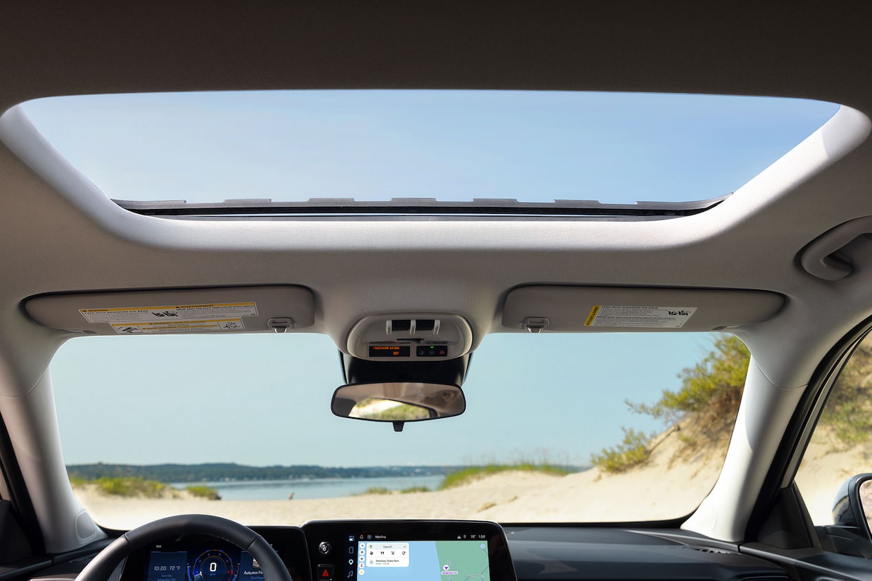 Interior view of the 2027 Chevrolet Trax small SUV showcasing the available sunroof, overhead console, and coastal scenery visible through the glass roof.