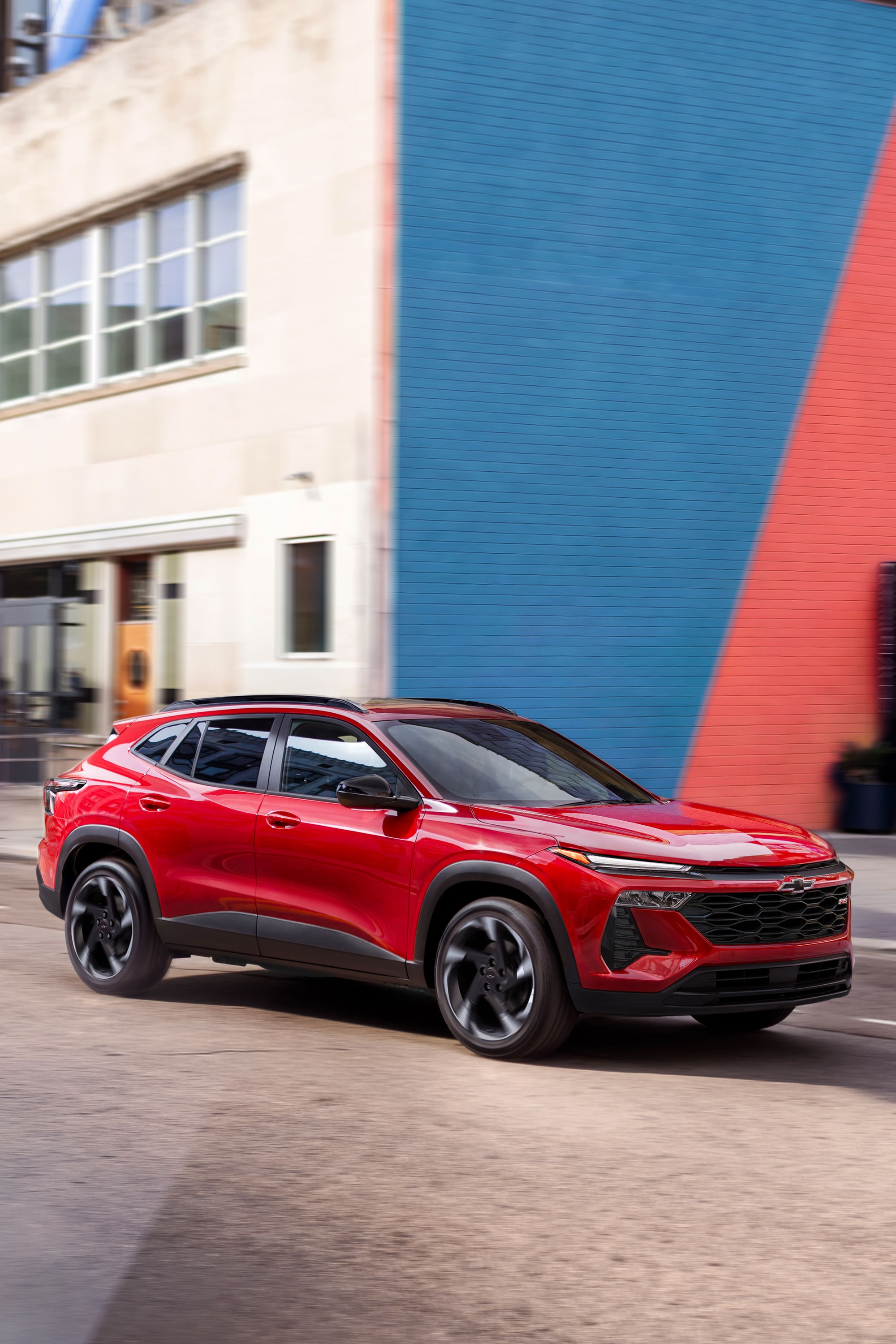 2027 Chevrolet Trax small SUV driving through an urban street with modern city buildings in the background.