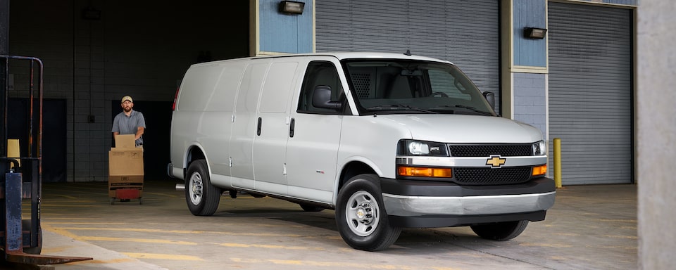 A man with boxes walks behind a 2022 Chevrolet Express Cargo Van.