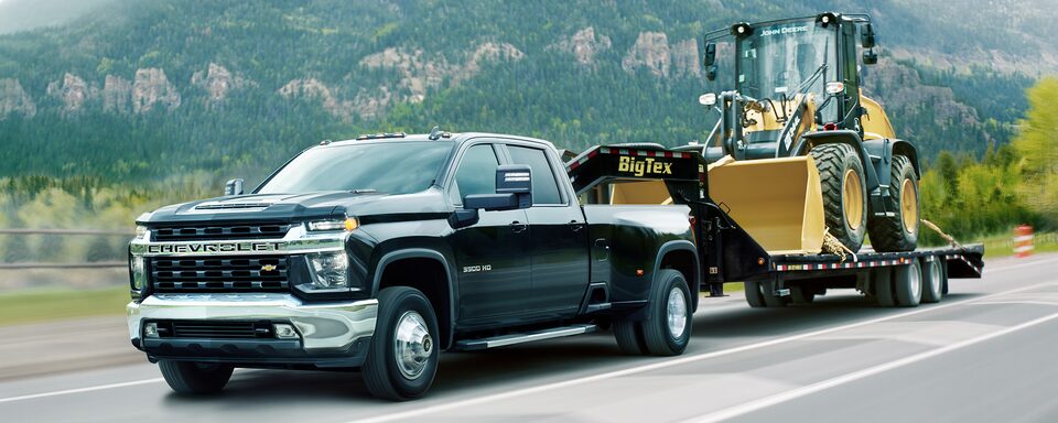 2023 Chevrolet Silverado HD towing heavy machinery down a road.
