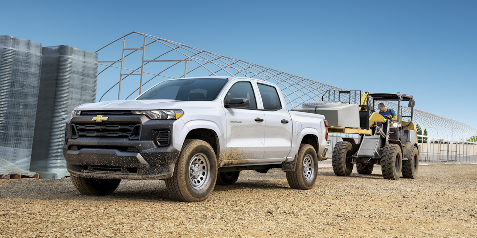 A forklift vehicle loading a heavy object into the cargo bed of the 2024 Chevrolet Colorado work truck.