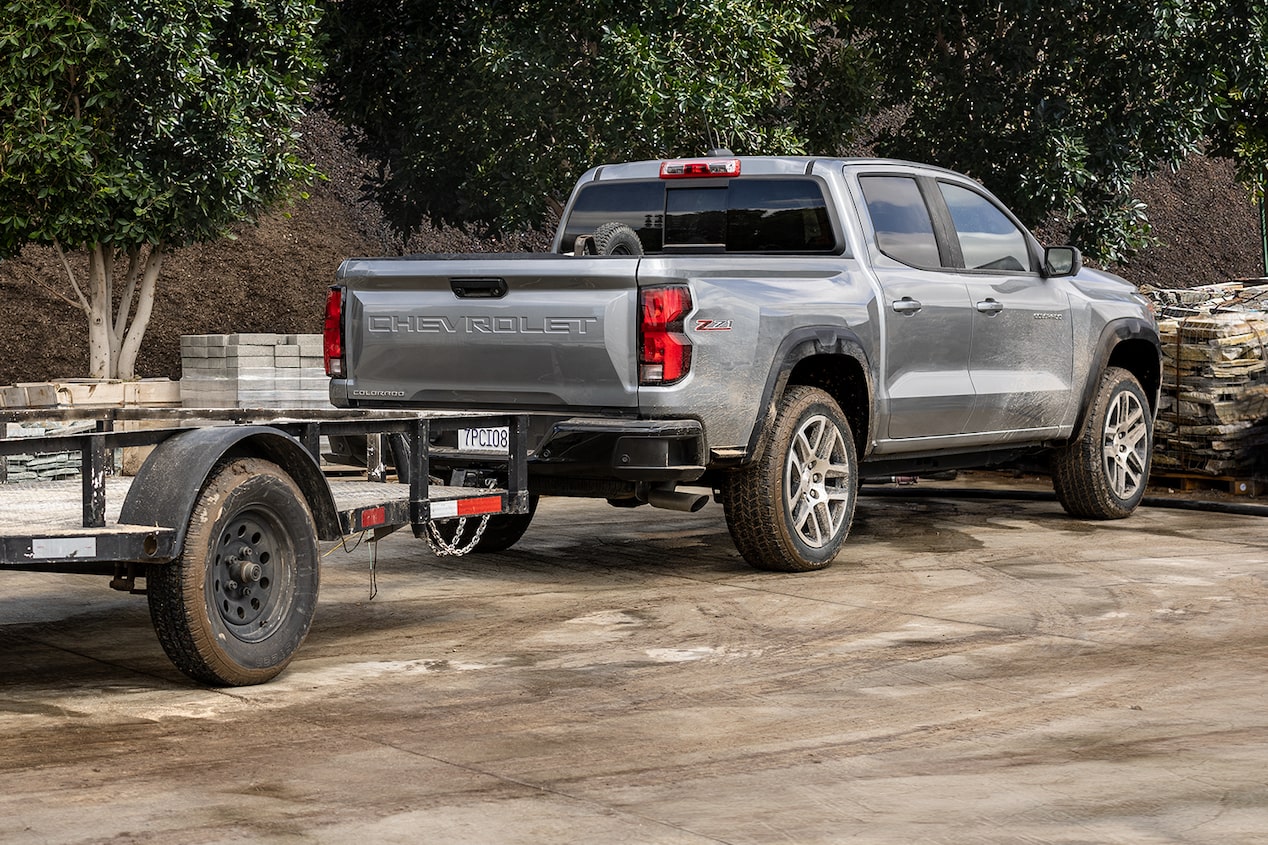 Back-side view of the 2024 Chevrolet Colorado work truck parked in a tree-lined dusty road.