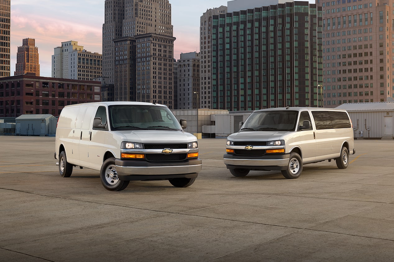 Two 2025 Chevy Commercial Express Vans Parked on Parking Garage Rooftop in a City