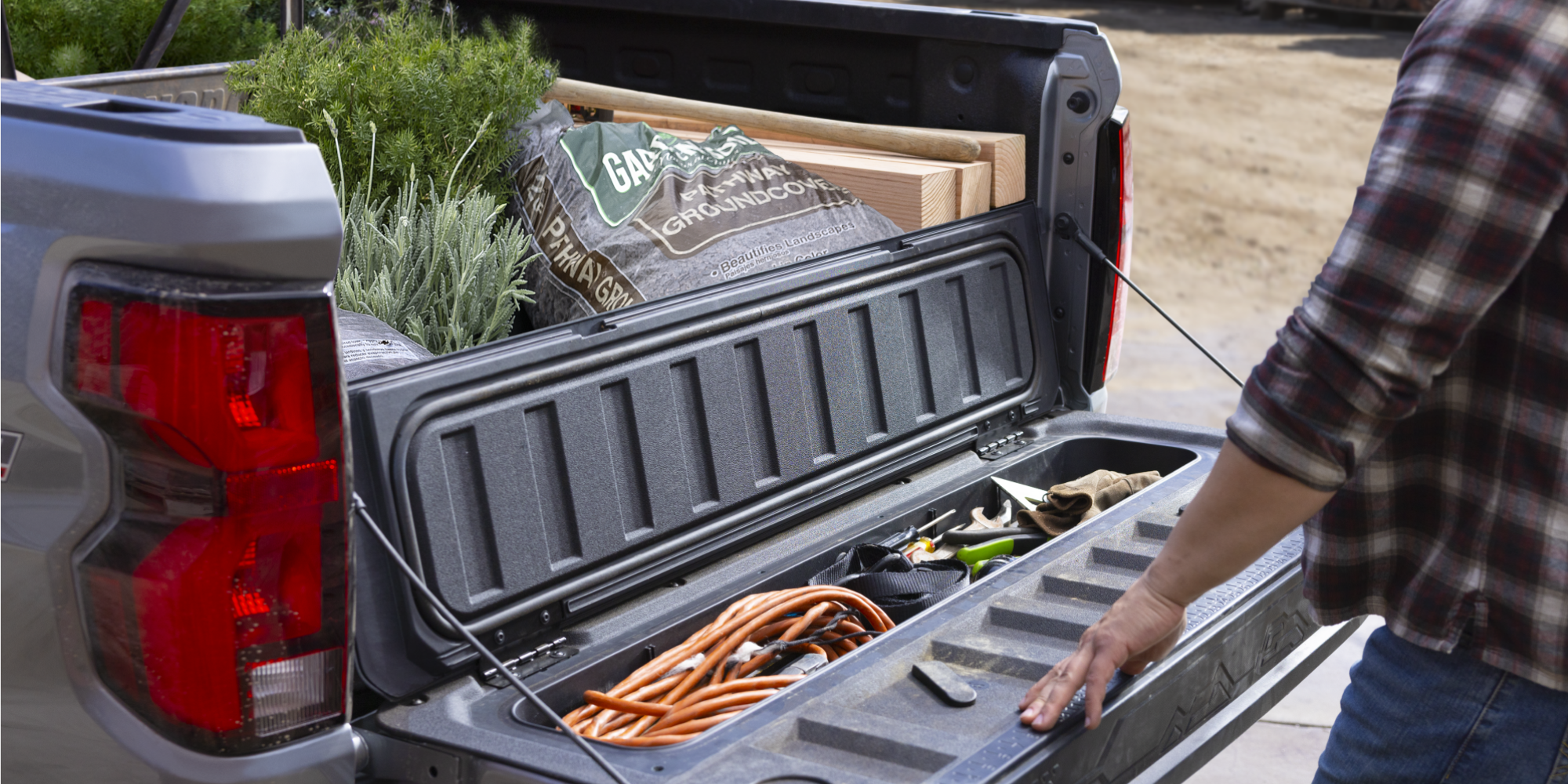A person opening a storage compartment on the cargo bed section of the 2026 Chevrolet Colorado Work Truck.