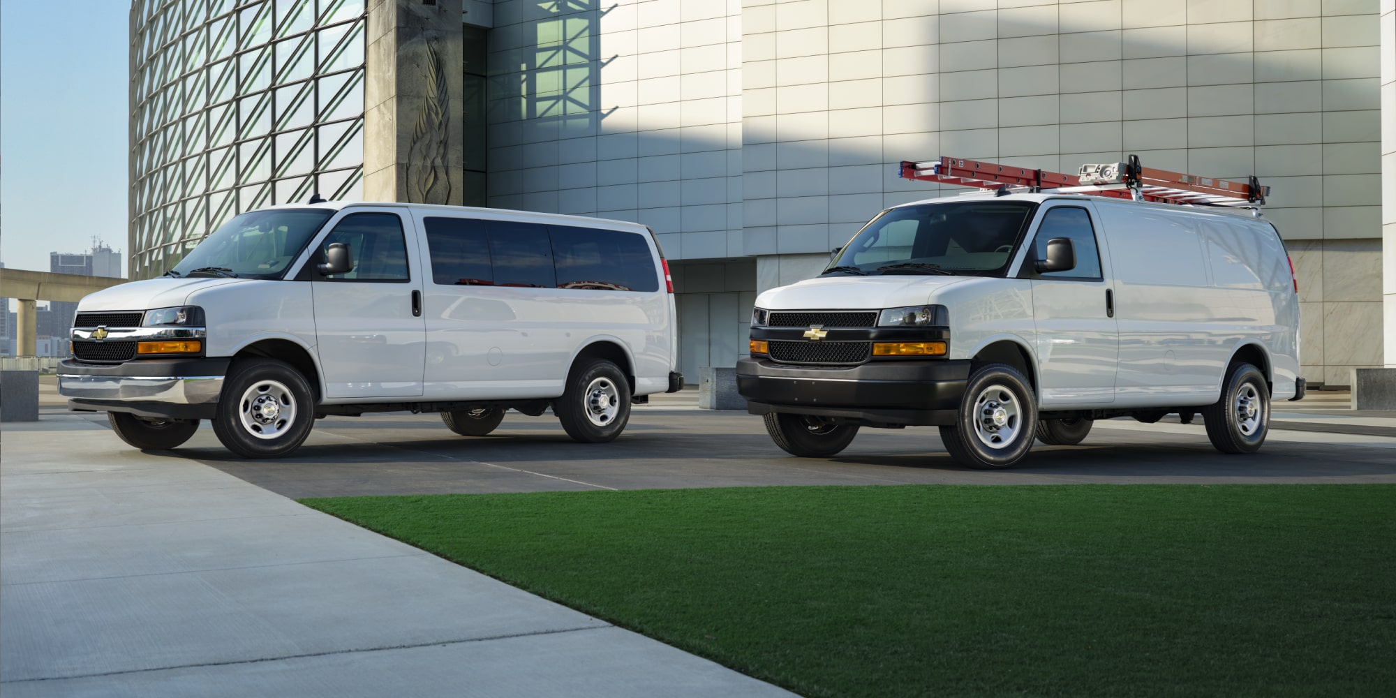 Deux fourgonnettes commerciales Chevrolet Express 2026 stationnées devant un immeuble de bureaux.